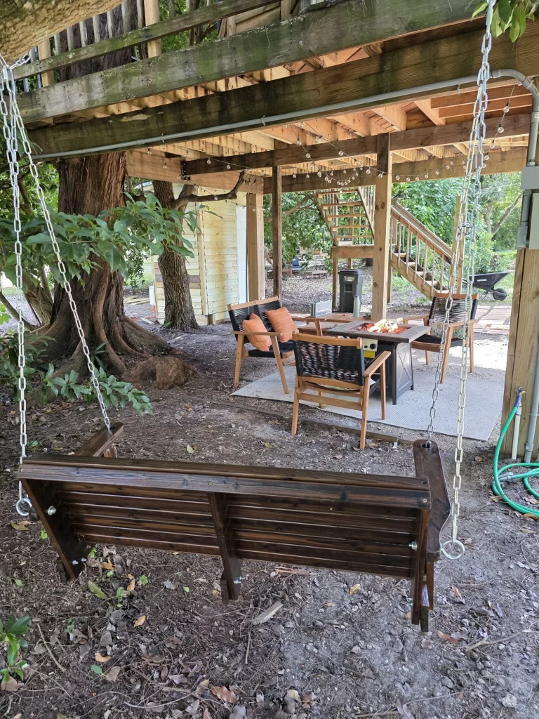 SunnyTops Treehouse exterior: a wooden swing overlooking a patio with seating, fire pit, and stairs, perfect for a treehouse