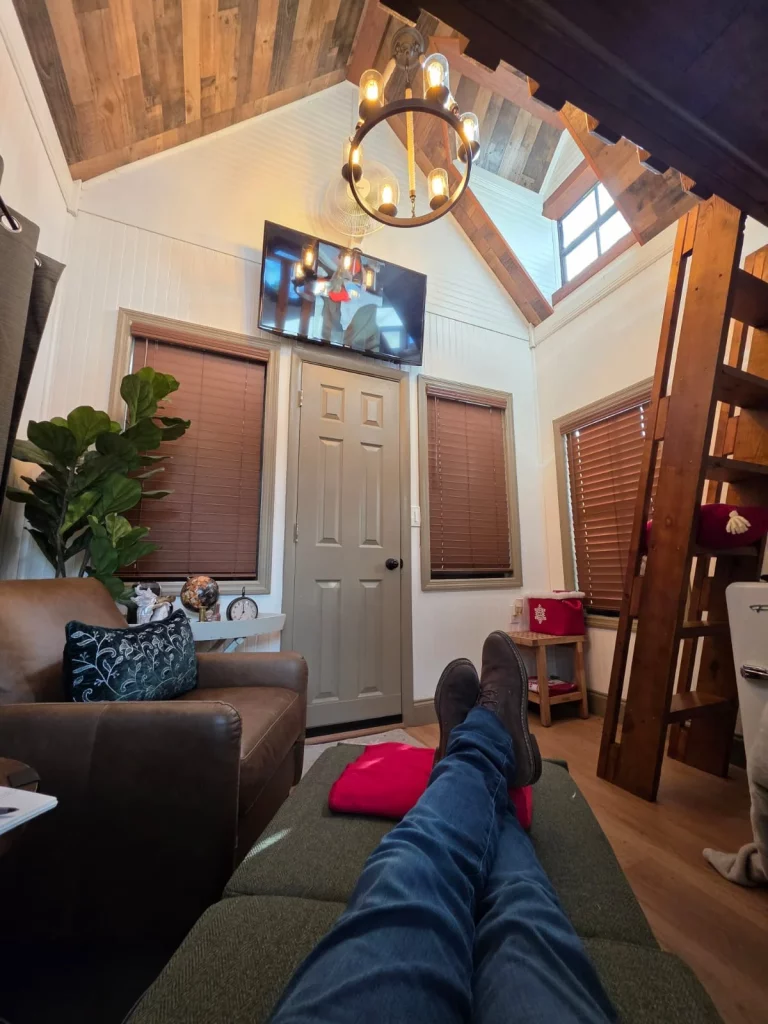 Cozy treehouse interior: Leather armchair, warm wood, TV, and ladder leading to a loft. Perfect for relaxing treehouse getawa