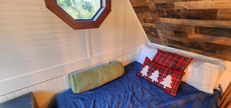 Cozy treehouse bedroom with plaid pillows, wooden accents, and an inviting window, perfect for a relaxing treehouse stay.