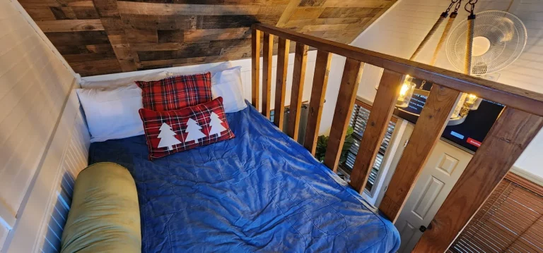 Cozy treehouse bedroom with a loft bed and plaid pillows, perfect for a romantic Florida treehouse getaway.