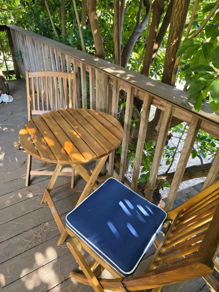 SunnyTops treehouse rental exterior with wooden deck, table, chairs, and lush green trees creating a peaceful, relaxing getaw