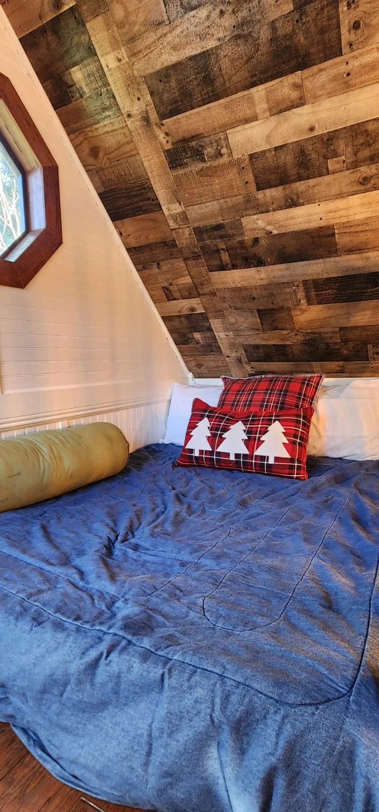 Cozy treehouse bedroom with blue bedding, plaid pillows, and rustic wooden walls, perfect for treehouse getaways in Florida.