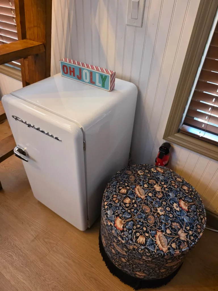 Charming treehouse rental interior with a retro mini-fridge, floral ottoman, and cozy decor for relaxing getaways in Florida.